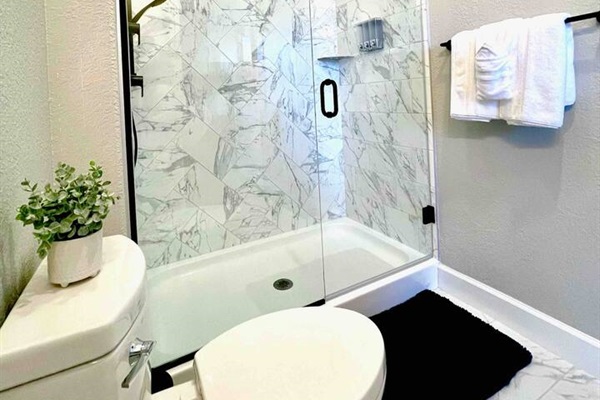 3rd Bedroom’s luxury bathroom, tiled to the ceiling, with overhead shower and hand wand, sink, and toilet. 