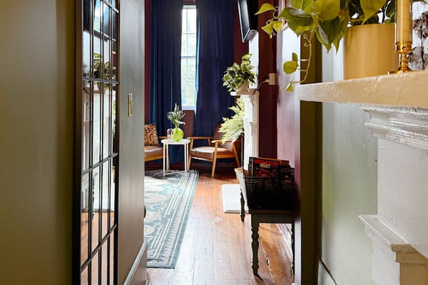 Historic hallway with original hardwood floors leading to the designer living room. This  charming New Orleans home blends classic architecture with bold modern interiors. 