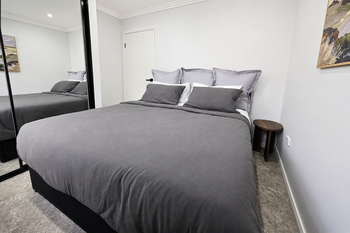 The side table sits beside the bed, with the mirrored wardrobe positioned along the opposite wall for easy access.