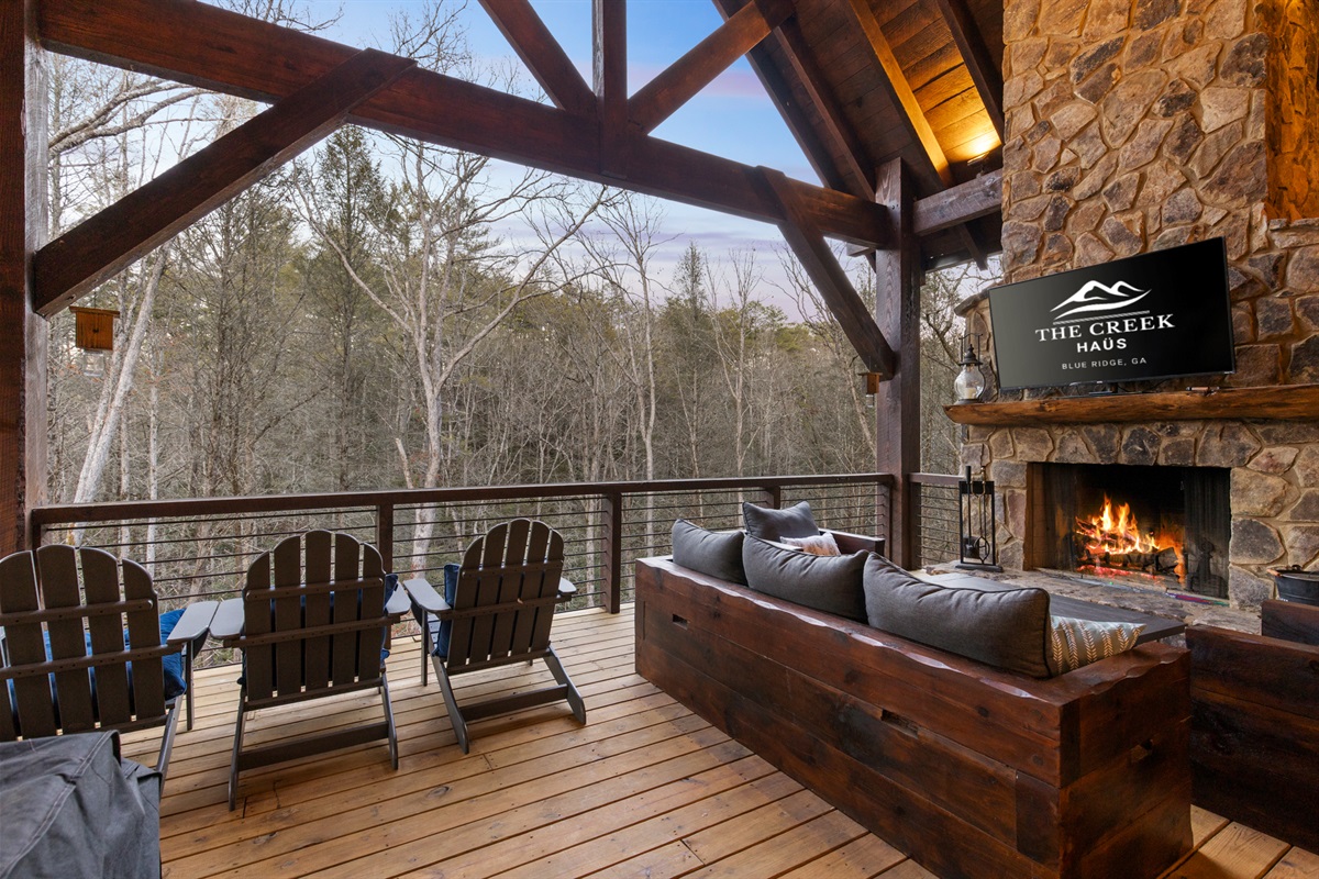Relax on the covered deck by the stunning stone fireplace, complete with plush seating and views of the surrounding woods.