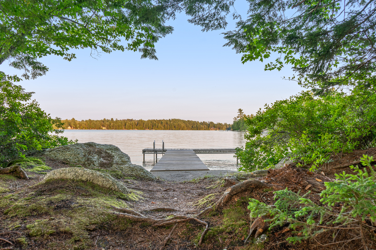 Path down to your private wooden dock at Loonrise Point! Features a swim ladder and concrete landing framed by natural granite rocks and pine roots. Tie up your boat, launch kayaks, or swim in clear Beech Hill Pond water in Otis, ME.