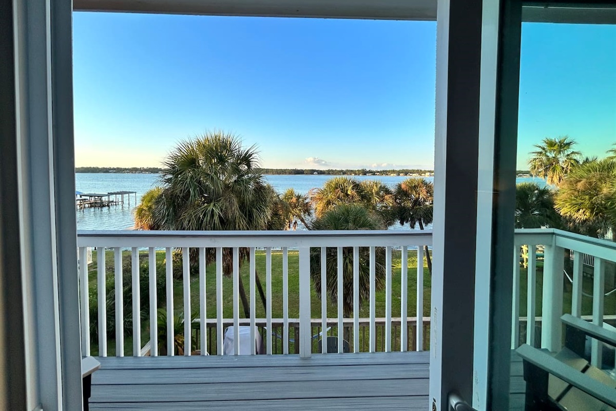 Tranquil balcony view with lush palm trees and sparkling waterfront serenity.