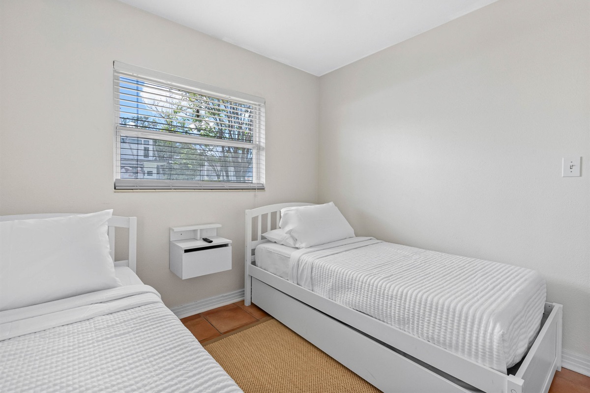 The room features two sturdy white twin beds, each outfitted with fresh, hotel-quality linens and plush pillows to ensure a restful night’s sleep.