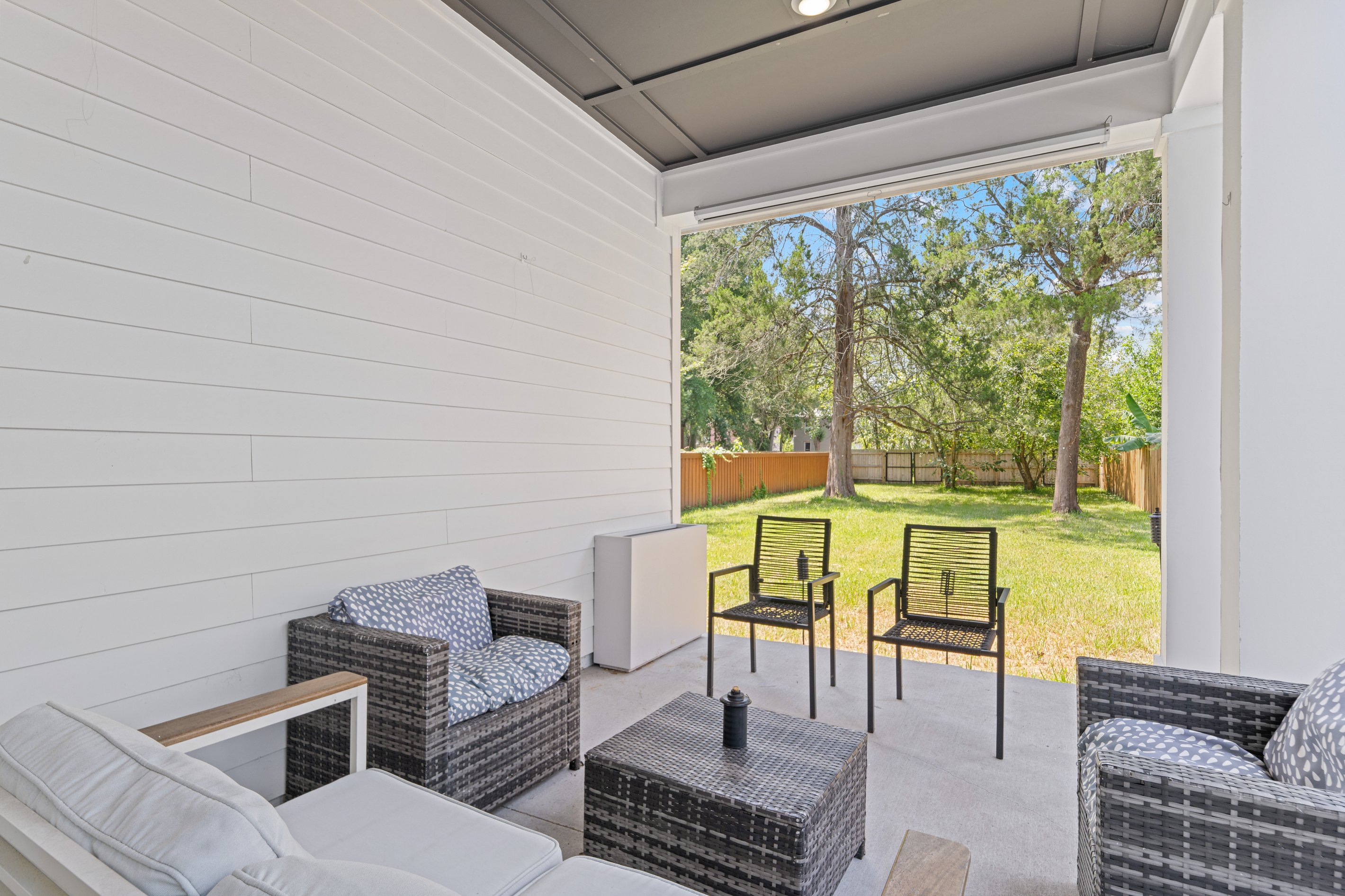 The shaded patio is where the evening lands. Coffee out here before anyone wakes, cards and cold drinks after dinner, the yard stretching green beyond. Sheltered from the sun, open to the breeze, made for lingering.