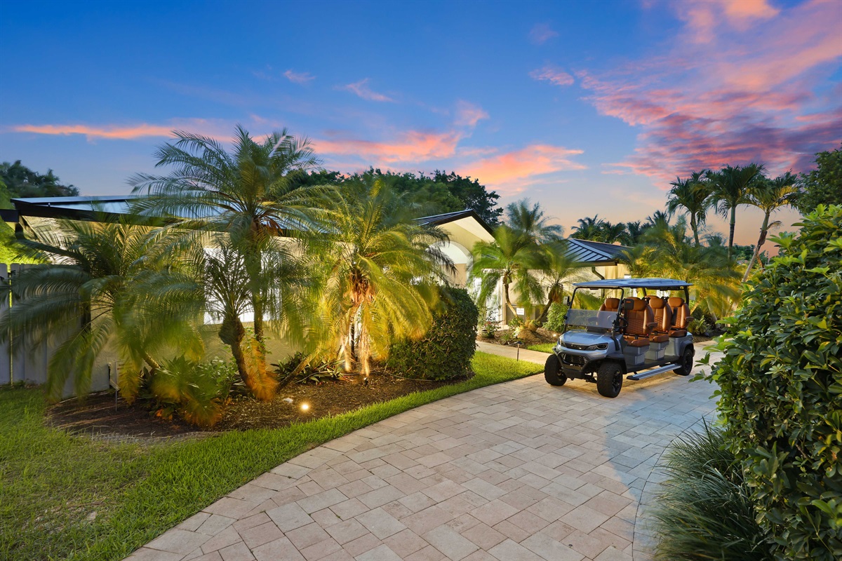 Arrive to golden-hour South Florida charm, with tropical palms, a lit entry, and the golf cart ready to make local exploring easy.