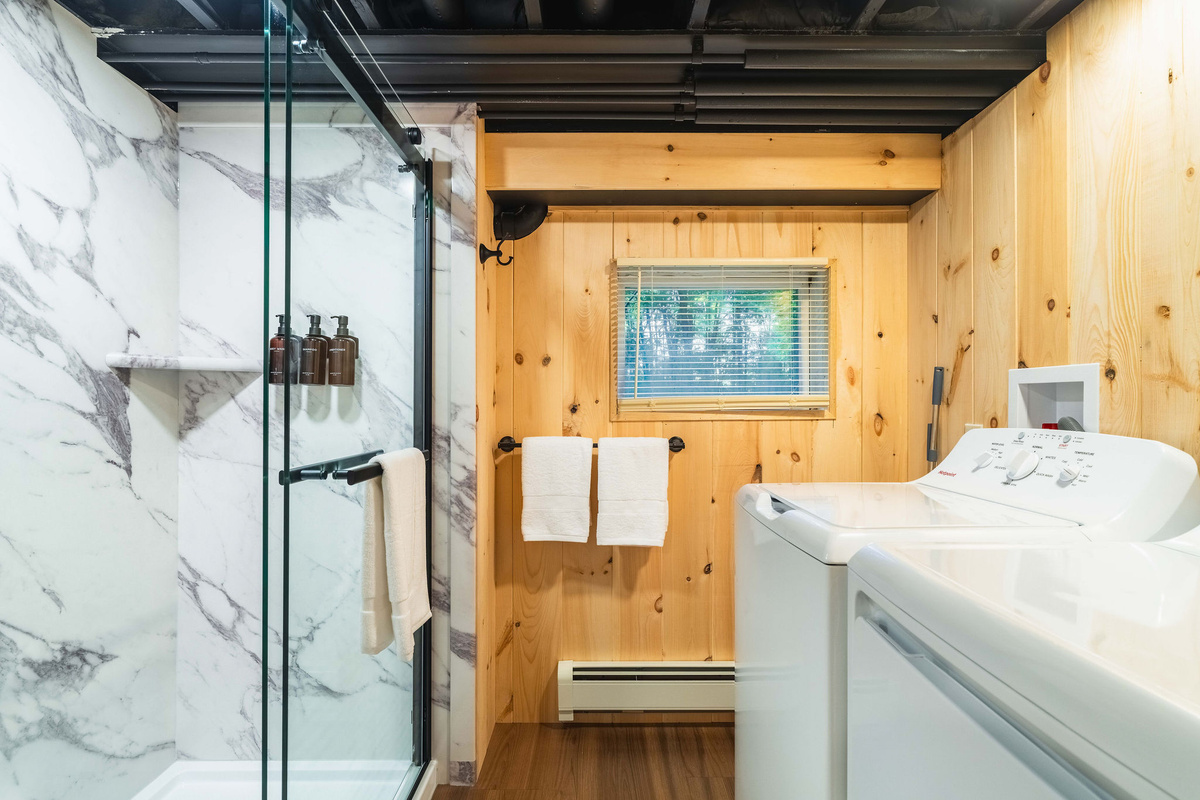 🚿 Lower-level full bath with a tiled walk-in shower — plus the first of two washer/dryer sets.