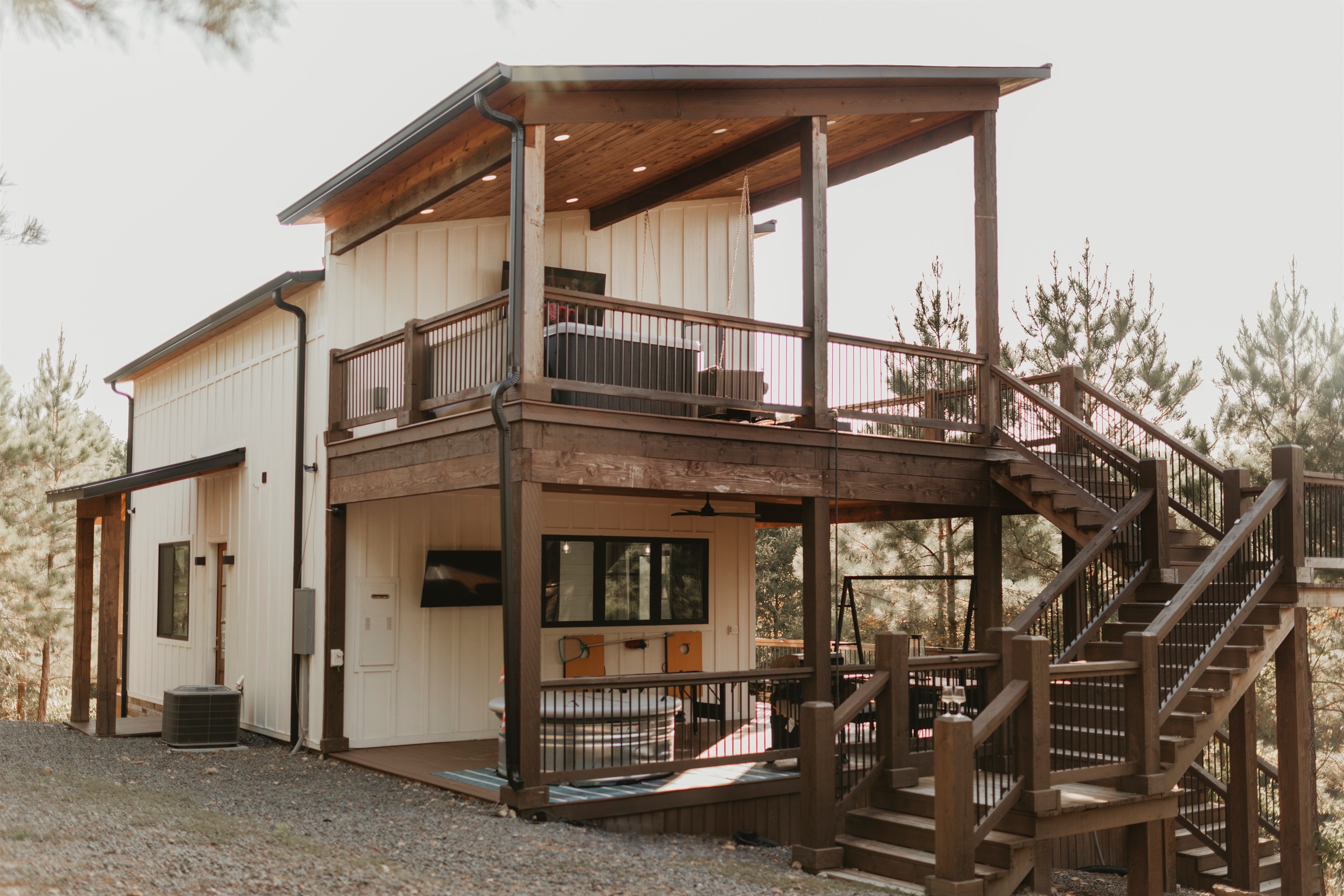 A modern cabin exterior with two levels of covered decks, outdoor seating, and forest views. Designed for gathering, grilling, and relaxing, it blends style and comfort with the beauty of nature.