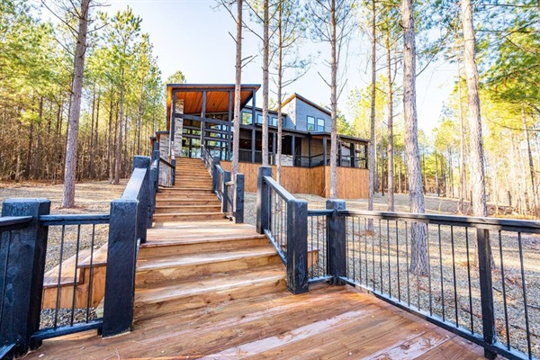 A breathtaking cabin entrance with grand wooden stairs leading to a luxury lodge surrounded by tall pine trees. This serene escape is perfect for nature lovers and outdoor enthusiasts.