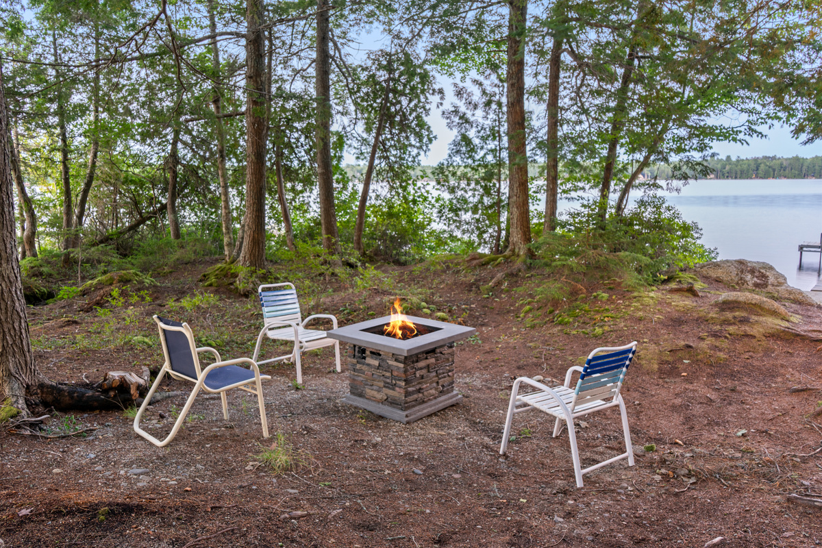 Unwind by the propane fire table at Loonrise Point! Outdoor seating on pine needle soil overlooking Beech Hill Pond with dock access on the right. Easy flame setup for quiet lake evenings under the trees in Otis, ME—no firewood gathering needed!