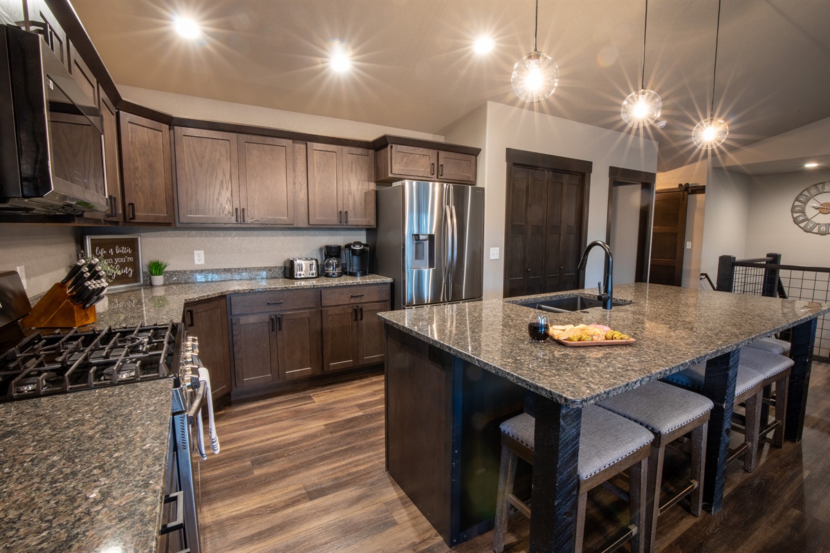 Prepare gourmet meals in the sleek kitchen at "On The Rocks," featuring a powerful gas stove, stainless steel appliances, and a spacious granite island with bar stools.