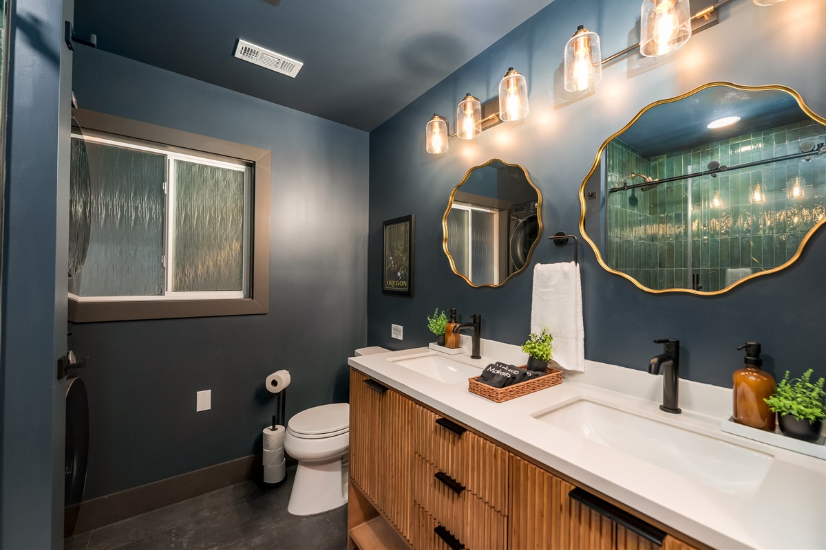 A stylish lower-level bathroom featuring a double vanity, warm wood accents, and a beautifully tiled shower—perfect for groups getting ready with ease.