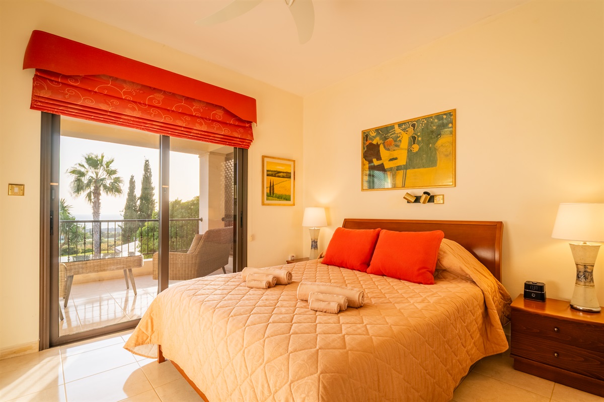 Master bedroom featuring a private balcony with stunning views of the Mediterranean and a full ensuite bath with a walk-in shower. The room has spacious closets, a ceiling fan, a dedicated AC/heating unit, and a Bluetooth-enabled speaker/alarm clock combo.