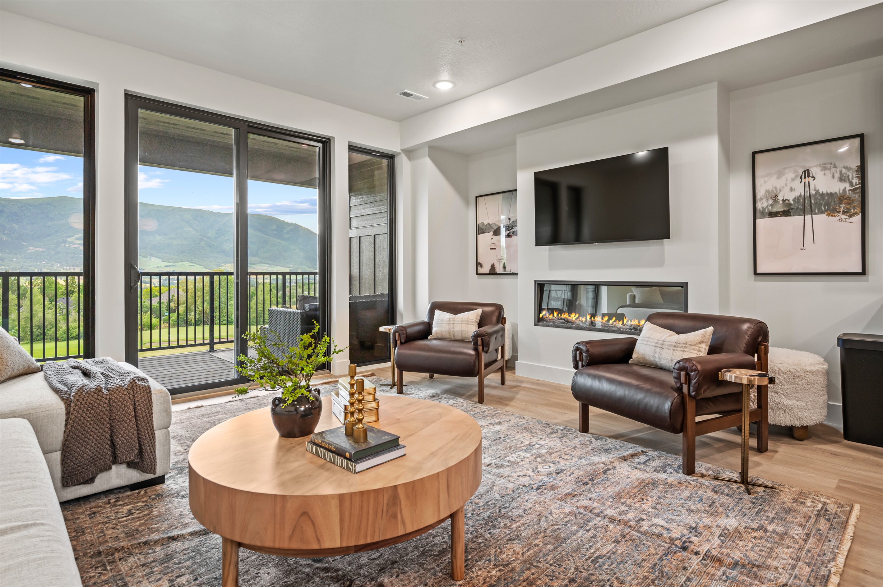 Floor-to-ceiling windows frame stunning mountain views, complemented by a sleek fireplace and modern décor.