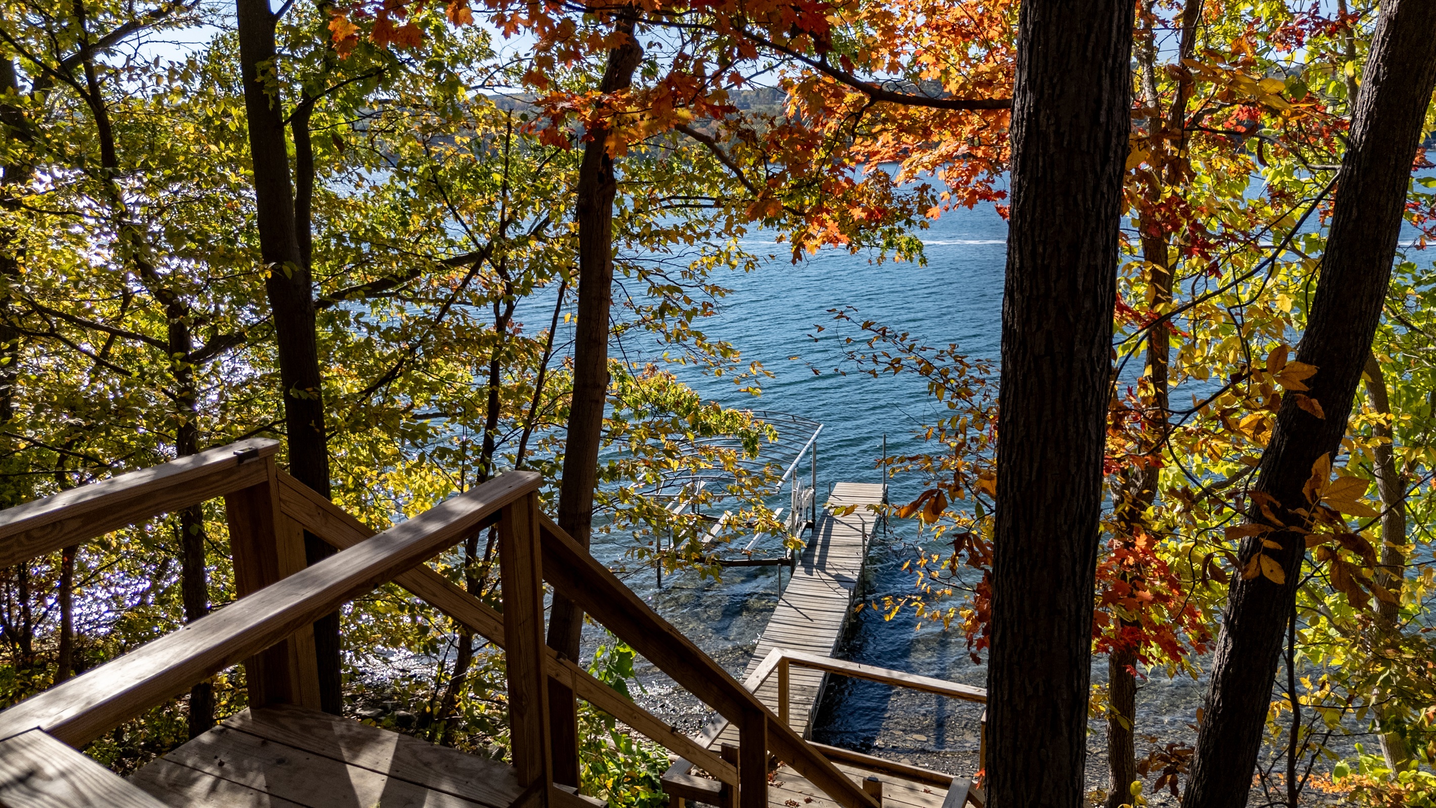 Tree-lined stairs leading to sand/stone beach and lakeside seating.