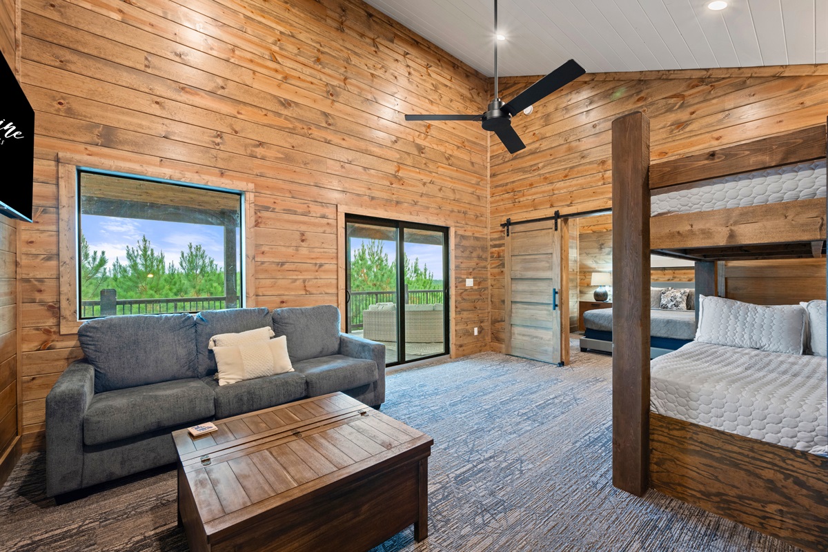 A warm upstairs space with a comfy sofa, rustic wood walls, and built-in bunk beds by the balcony doors.