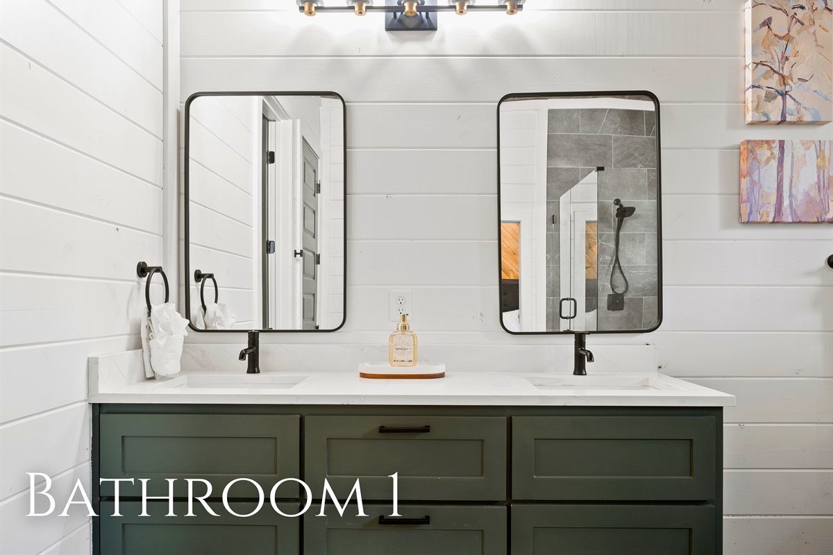 Streamlined double vanity with sleek mirrors and modern black fixtures set against a backdrop of white paneled walls and a green cabinet.