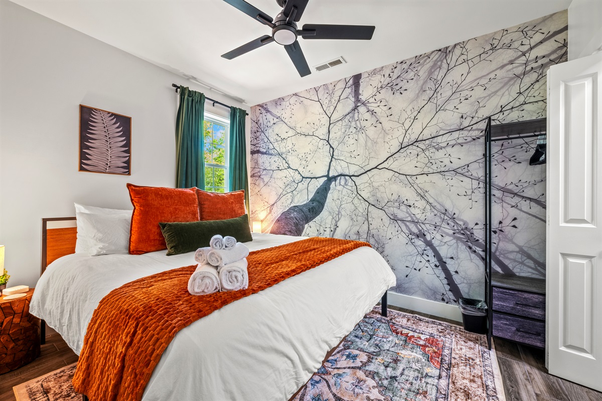 This cozy lower-level bedroom features a king-size bed beneath a peaceful tree canopy mural, plus a twin-over-twin bunk—ideal for families or groups needing flexible sleeping arrangements in a compact but comfortable space.