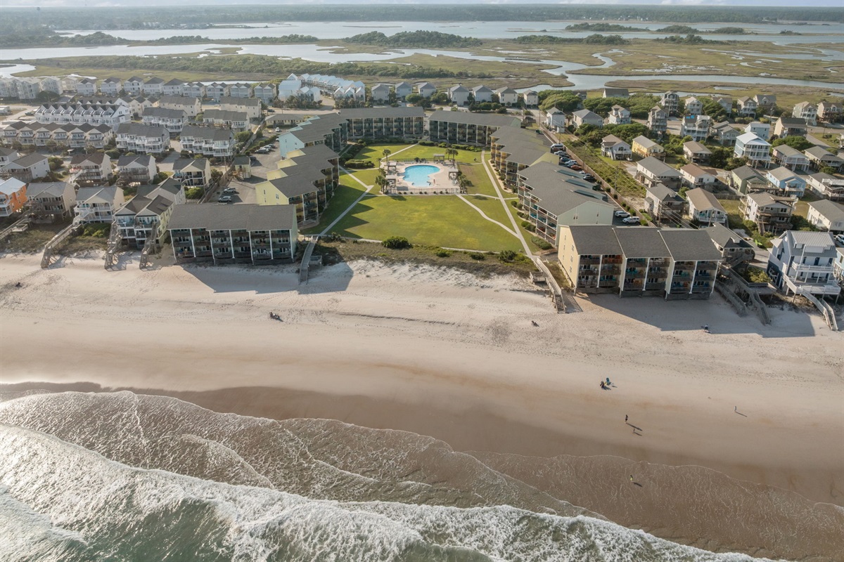 Aerial view of Surf Condos with pool, green space, and beachfront location