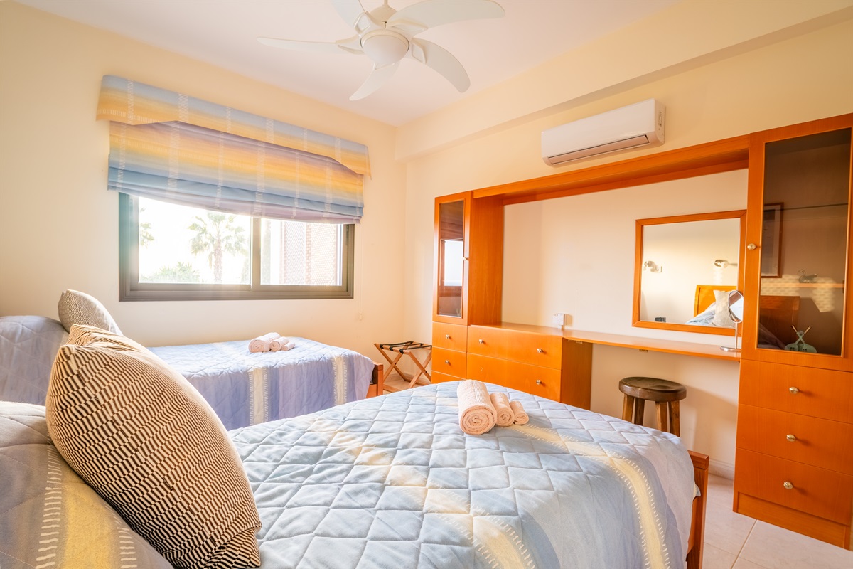 Twin bedroom with a window facing the back garden and swimming pool. The room has spacious closets, a ceiling fan, a dedicated AC/heating unit, and a Bluetooth-enabled speaker/alarm clock combo.