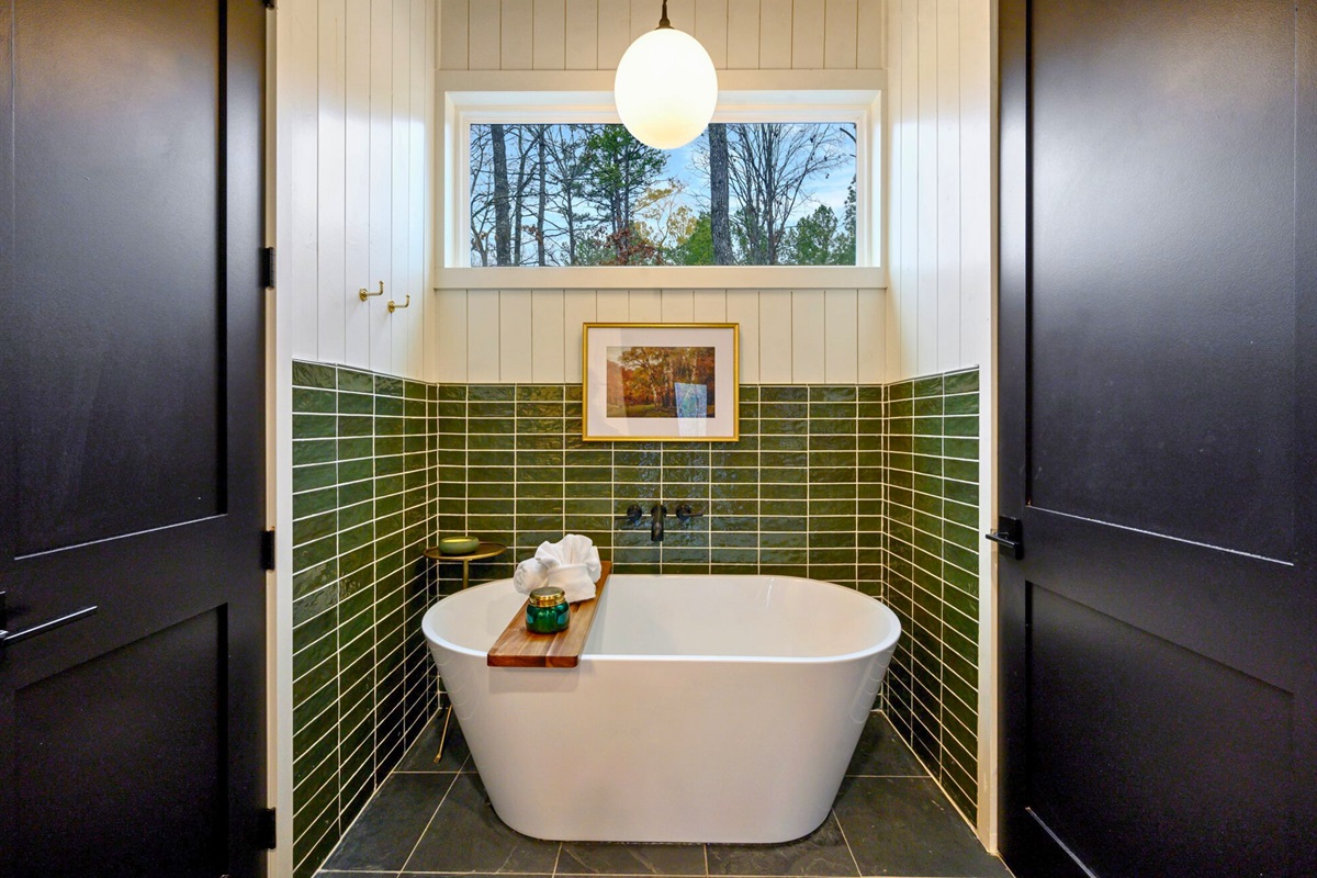 The freestanding tub sits beneath a bright window, offering a peaceful spot for a quiet soak.