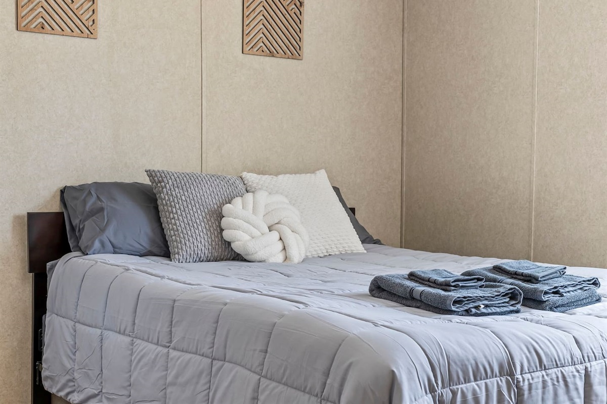 Inviting sleeping area featuring plush bedding, decorative pillows, and neatly prepared towels for your stay.