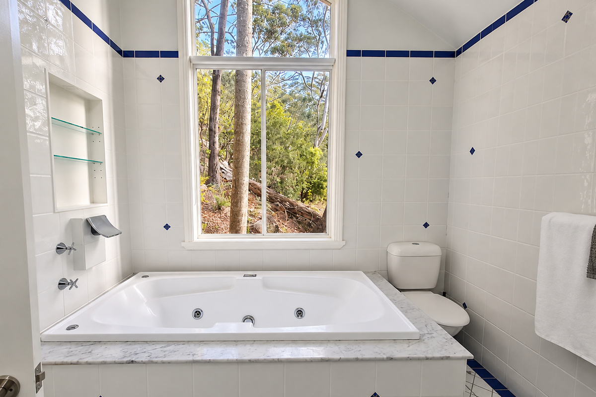 The upstairs bathroom at Carinya Coastal Escapes includes a deep spa bath, tiled surrounds and a large window looking out to the trees.