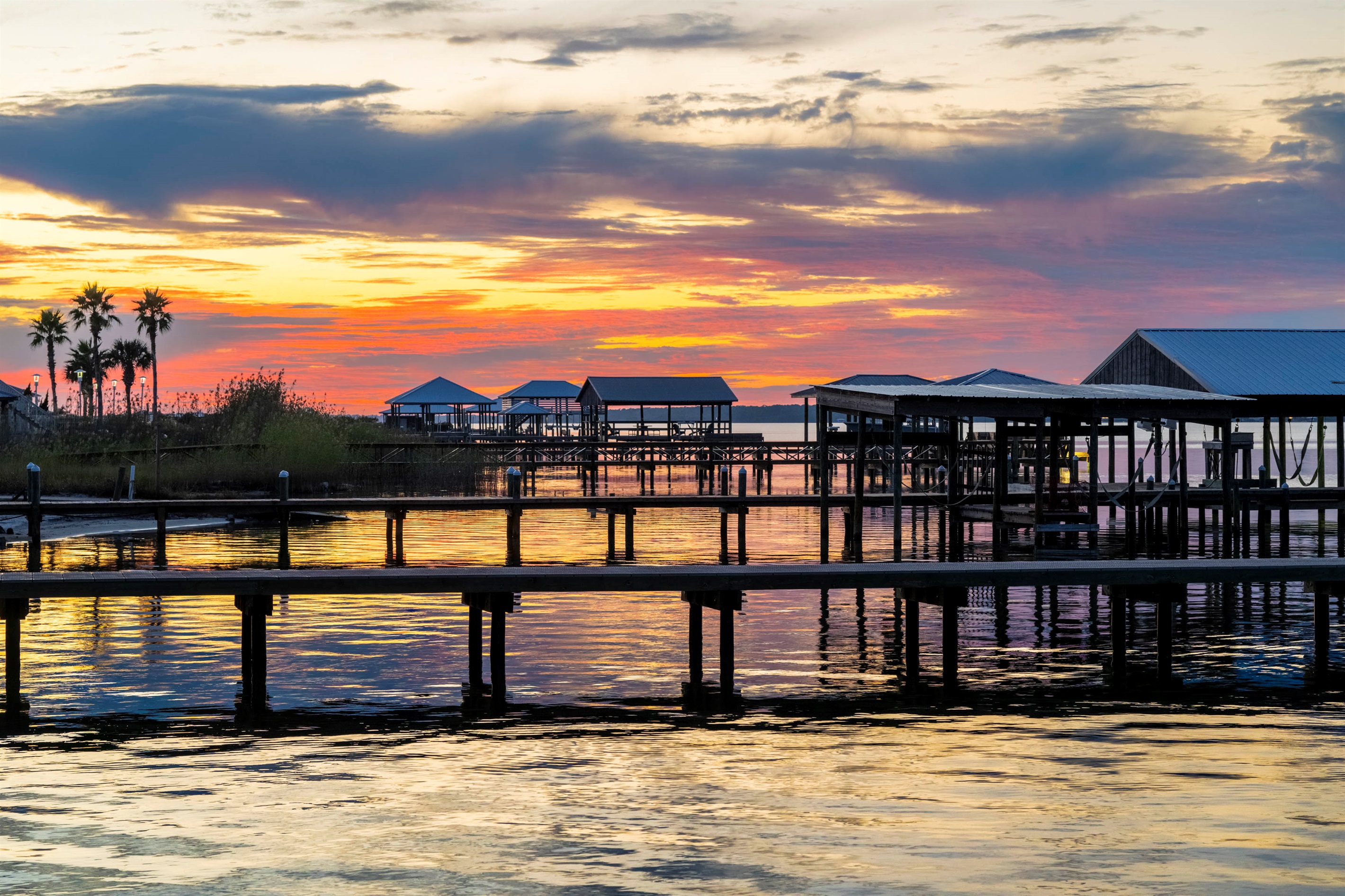 Golden sunset over tranquil waterfront homes with tropical palm trees.