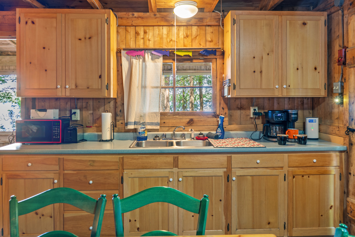 Fully equipped kitchen counter at Loonrise Point! Features dual coffee maker with mugs ready, microwave, toaster, double sink, & pine storage cabinets. Convenient setup for easy meal prep on Beech Hill Pond in Otis, ME.