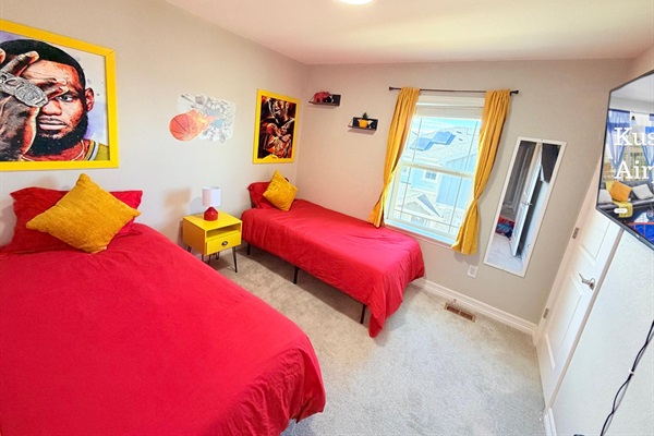 Upstairs bedroom with two twin beds, fun sports themed artwork, and a TV mounted across from the beds so guests can relax and watch shows in comfort.
