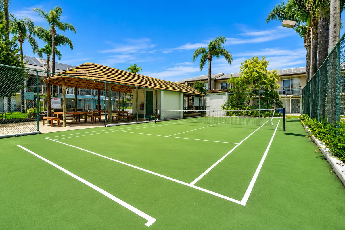 The tennis court adds an active outdoor option to the Sea Breeze Apartment complex, with palms and open sky around the shared space.