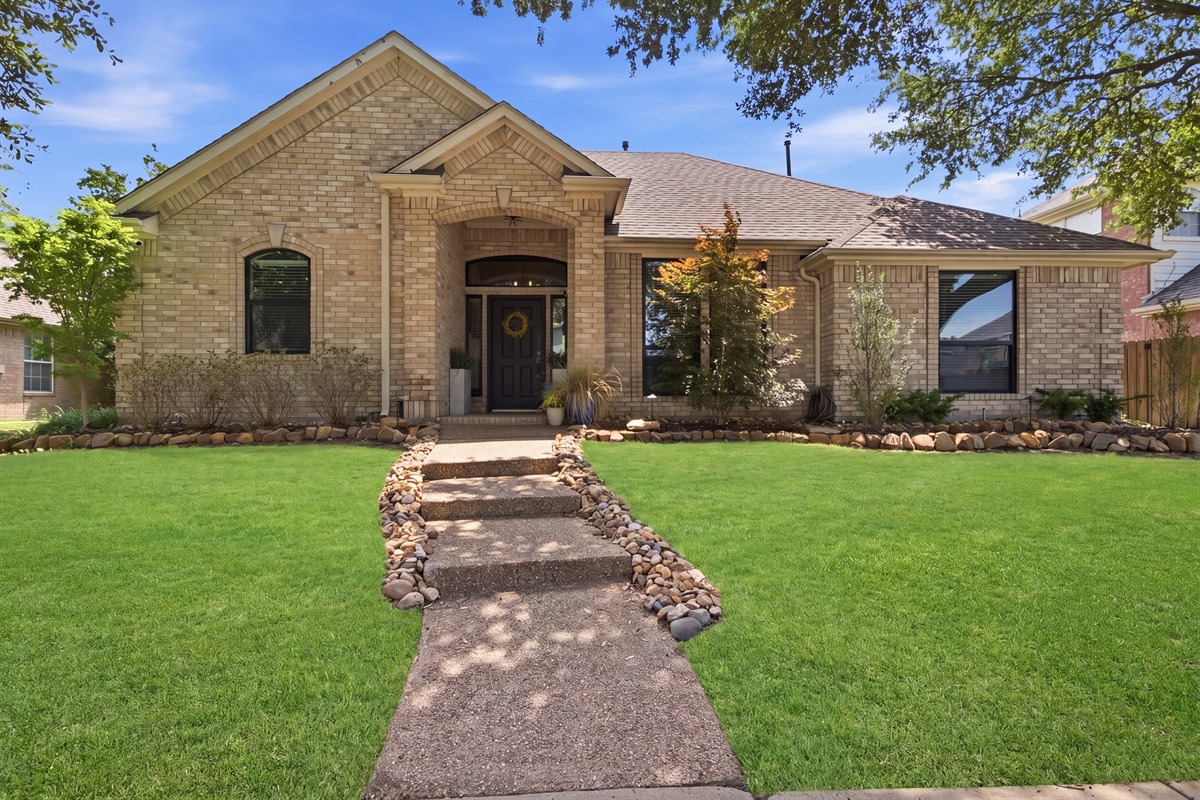Welcoming brick Exterior with manicured landscaping, stone walkway, and a quiet residential setting in The Colony, minutes from Grandscape and Stonebriar Country Club.
