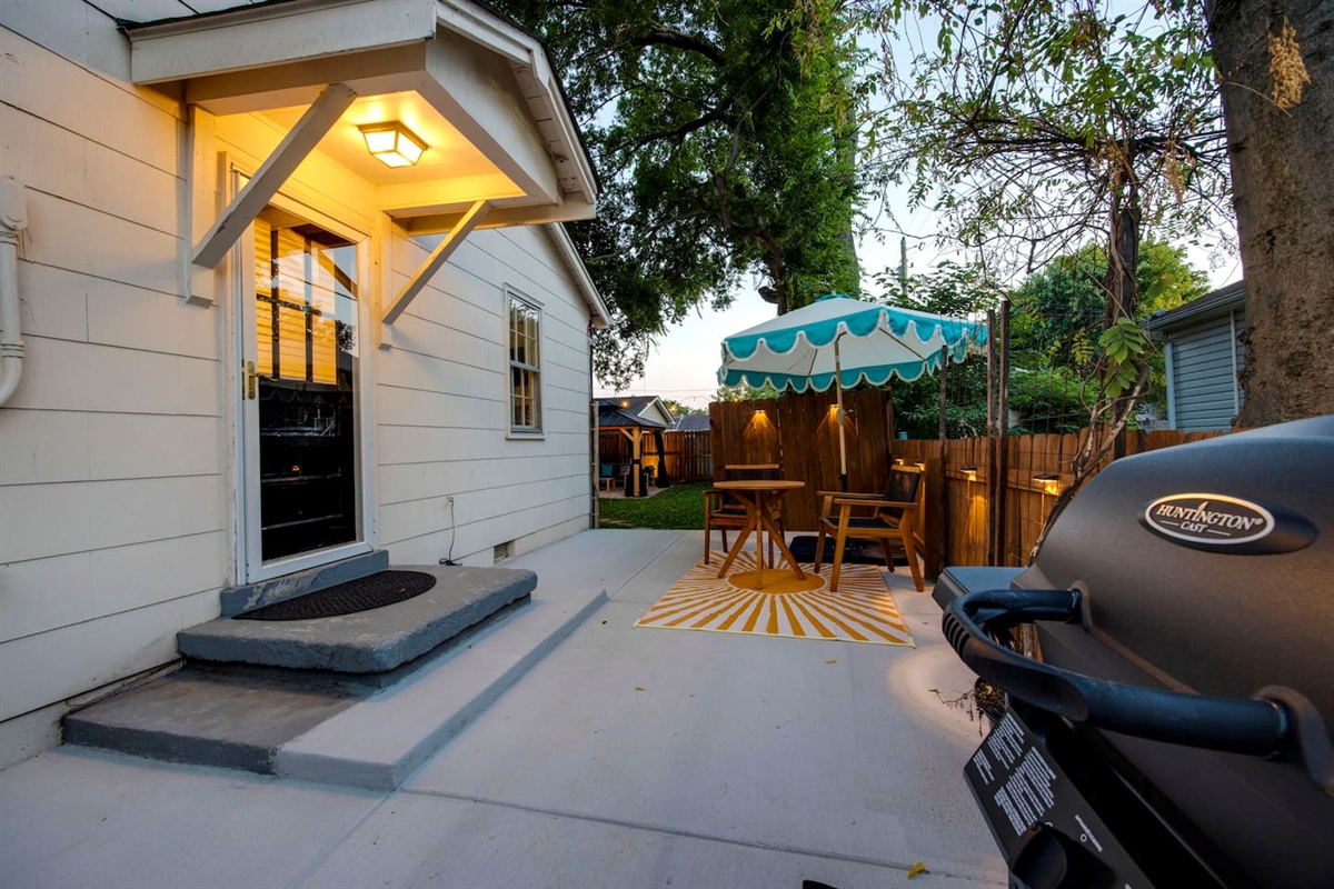 Side patio with cafe table and propane BBQ grill, leading into the fully fenced backyard.