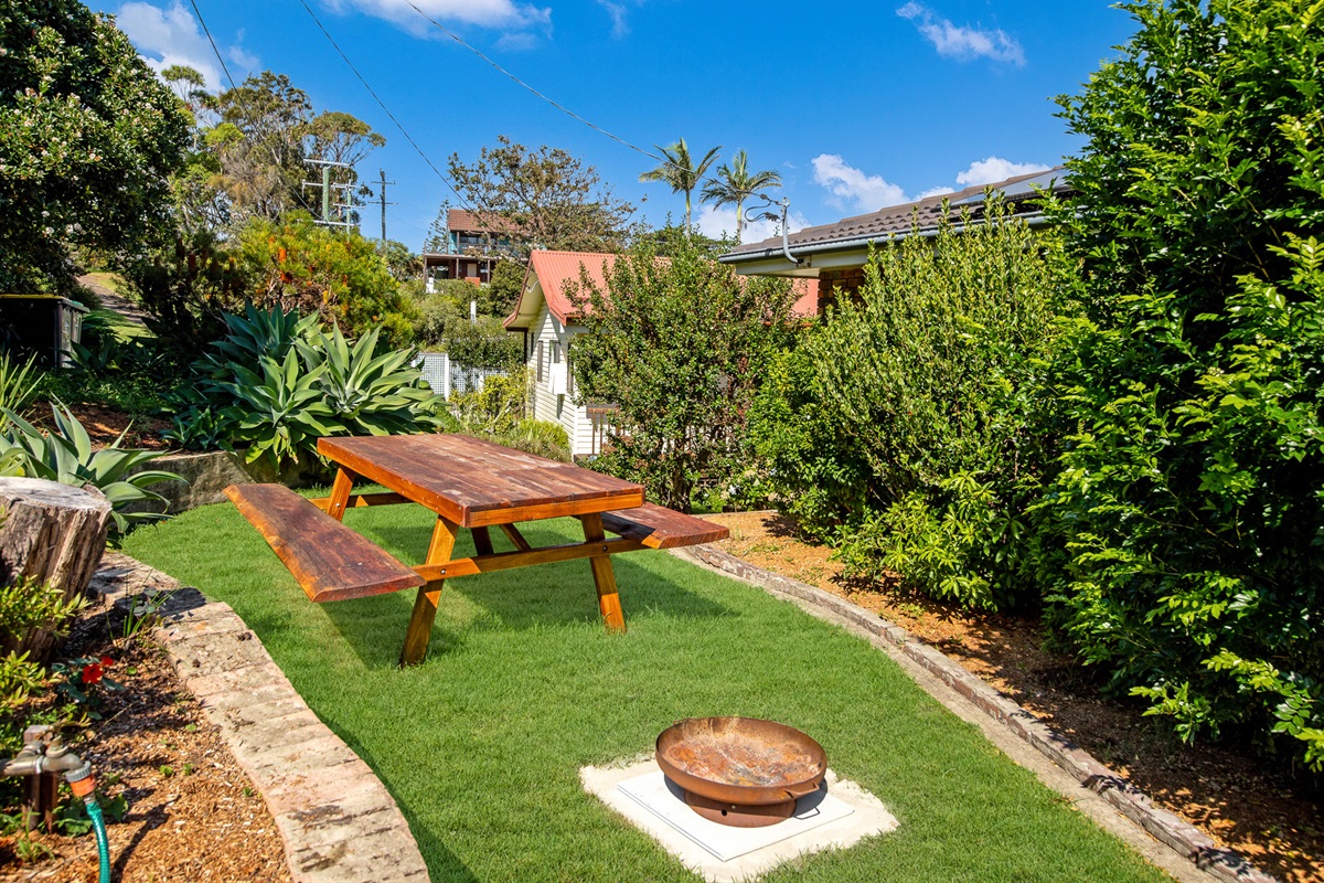 A firepit beside the outdoor table gives this garden space a strong beach-house feel, with greenery around the yard at Bertie’s 3 Beaches.