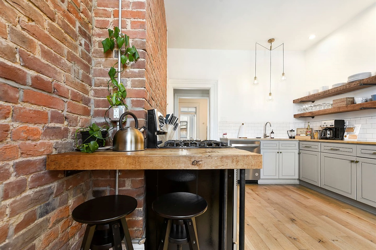 Enjoy a stylish kitchen with a cozy brick wall, fully equipped with cookware, appliances, and a coffee maker—perfect for your morning brew. Cook with ease and enjoy a warm, inviting space for your meals.