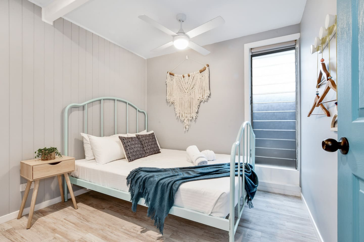 Aqua detailing, soft timber tones and a woven wall feature give this bedroom at Aaron's Beachside Boat House distinctive beach-house character.