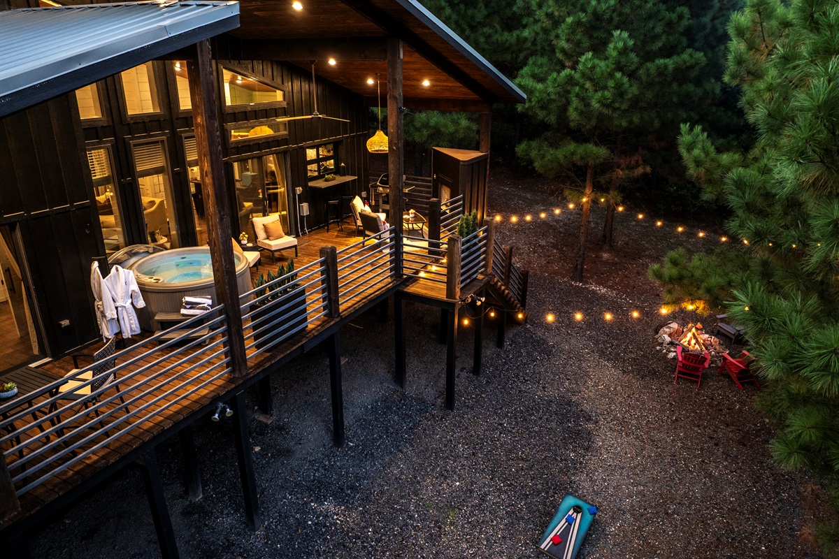 Modern cabin meets nature: hot tub, fire pit, and private deck surrounded by forest views and soft evening lights.