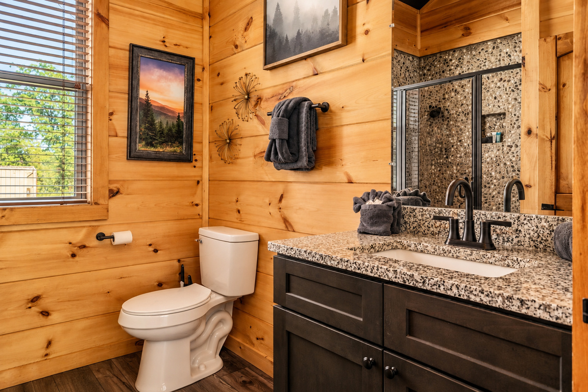 Roomy vanity, plush towels, bronze fixtures, and a sunny window onto the woods.