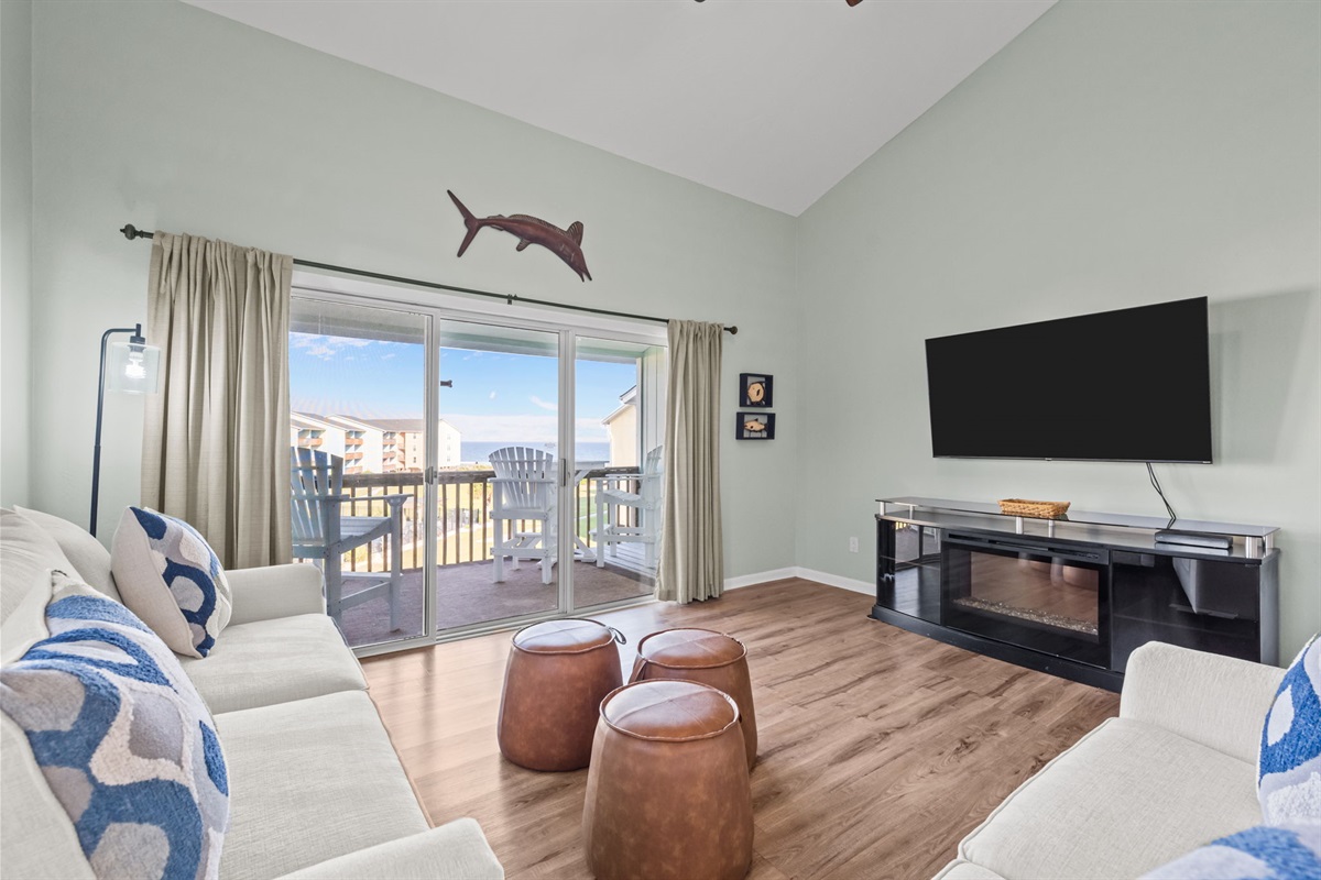 Bright coastal living room with vaulted ceilings, smart TV, and direct balcony access with ocean views
