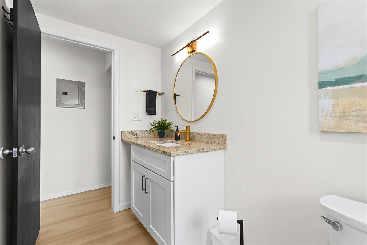Vanity area with gold-accented round mirror and granite countertop—both stylish and practical.