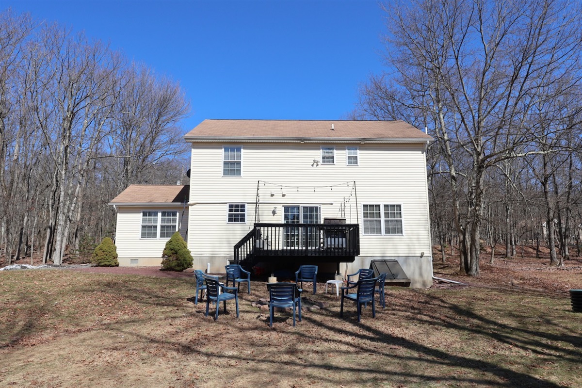 Backyard, as seen facing the house. Firepit area with 8 chairs. Surrounded by trees.