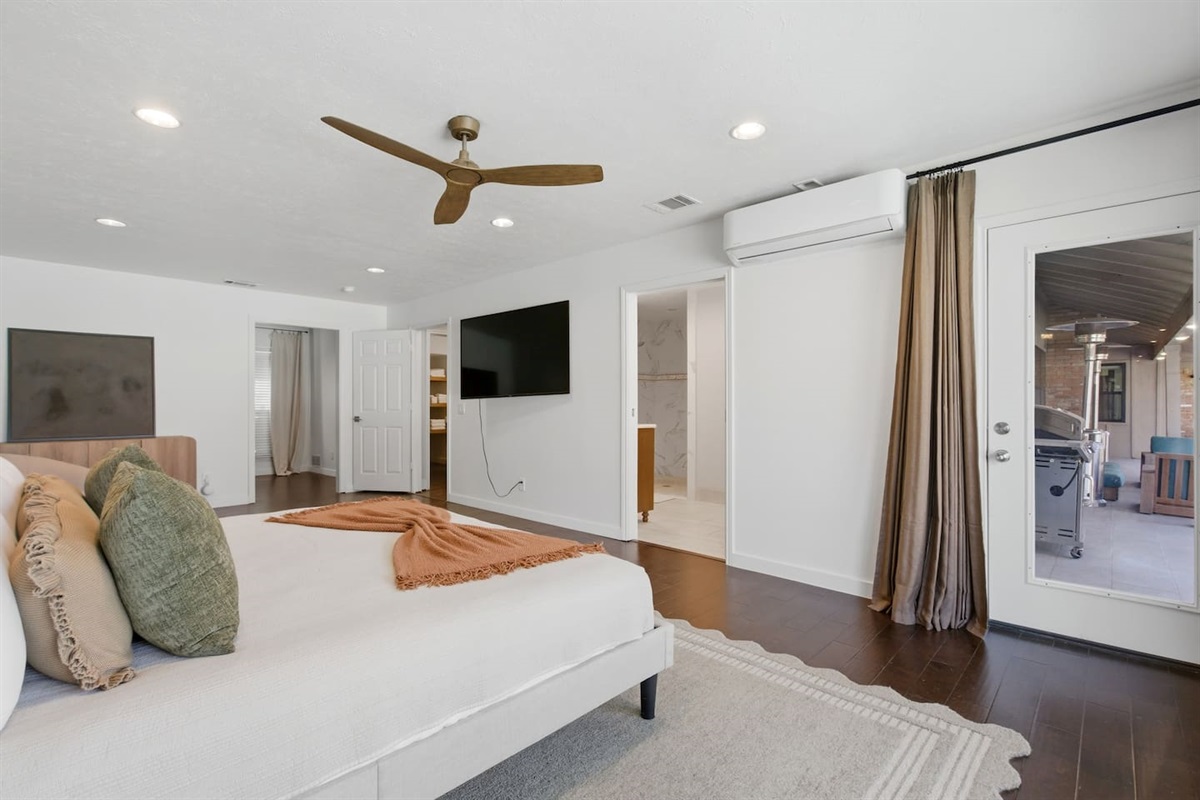 Luxe primary bedroom with a king bed, 65” Smart TV, ceiling fan, full-length mirror, cozy sitting area, room-darkening shades, and direct access to the private backyard.