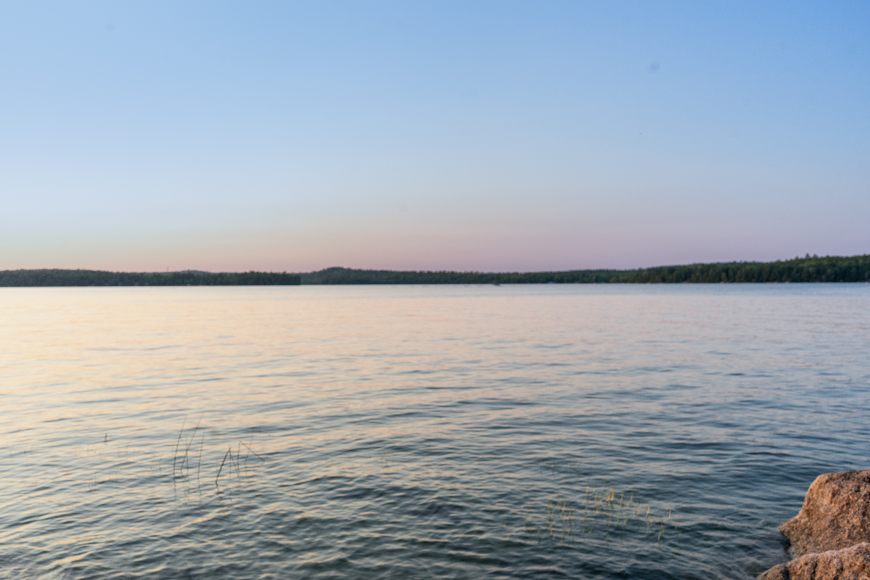 East-side shoreline view at Loonrise Point! Soft dusk sky over clear, calm waters with granite ledge and aquatic grasses. Experience pristine, private peninsula lakefront on Beech Hill Pond in Otis, ME—ideal for swimming, kayaking, and relaxation.