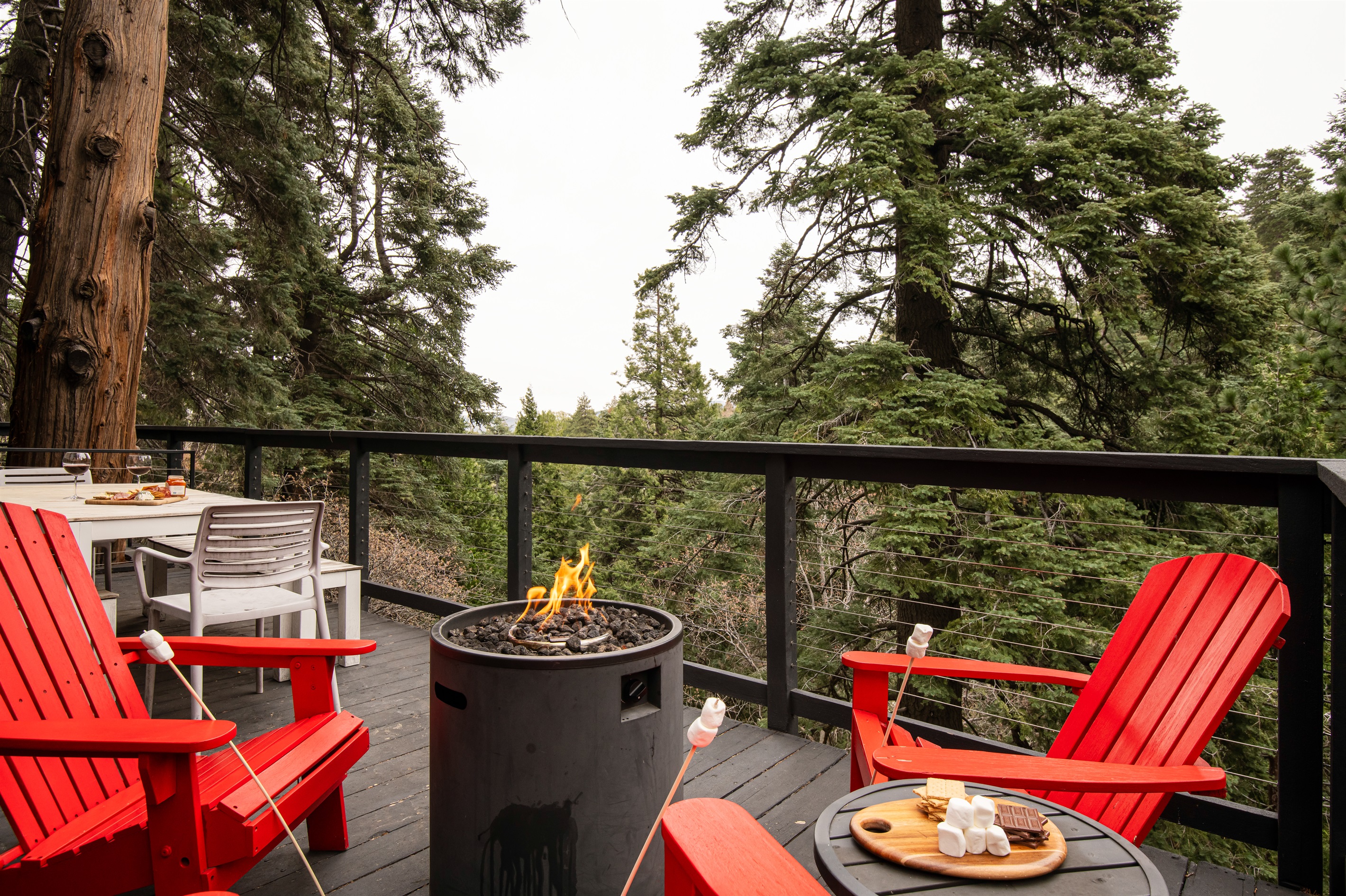 Outdoor fire pit with Adirondack seating and forest views—perfect for cozy nights, s’mores, and relaxing during your Lake Arrowhead cabin stay.