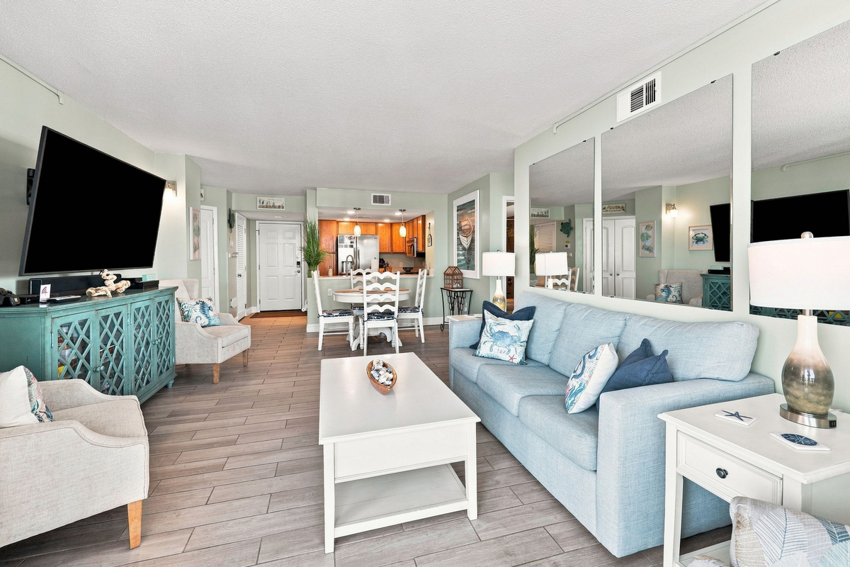 Spacious living room featuring a plush sofa, large wall-mounted flat-screen TV, and mirrored accents that brighten the space.