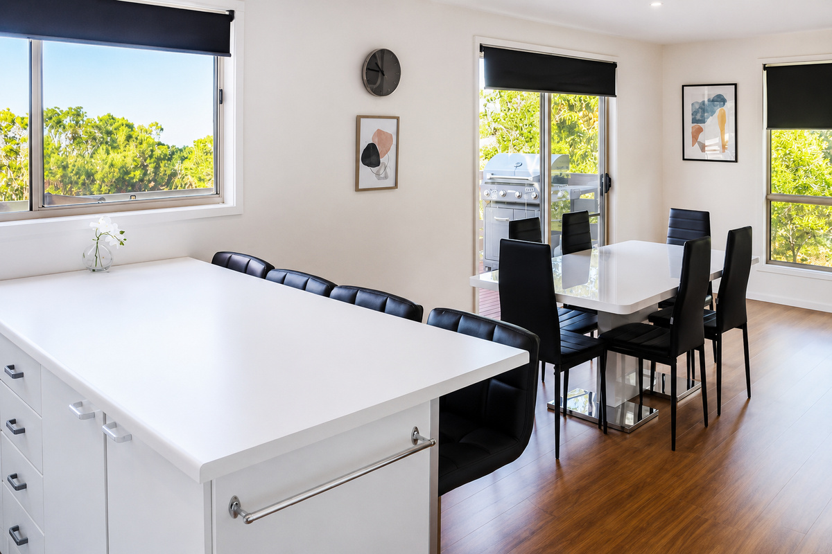 The kitchen island and dining area at Carlenes Getaway open onto the balcony, with leafy Loch Sport outlooks from both sides of the room.