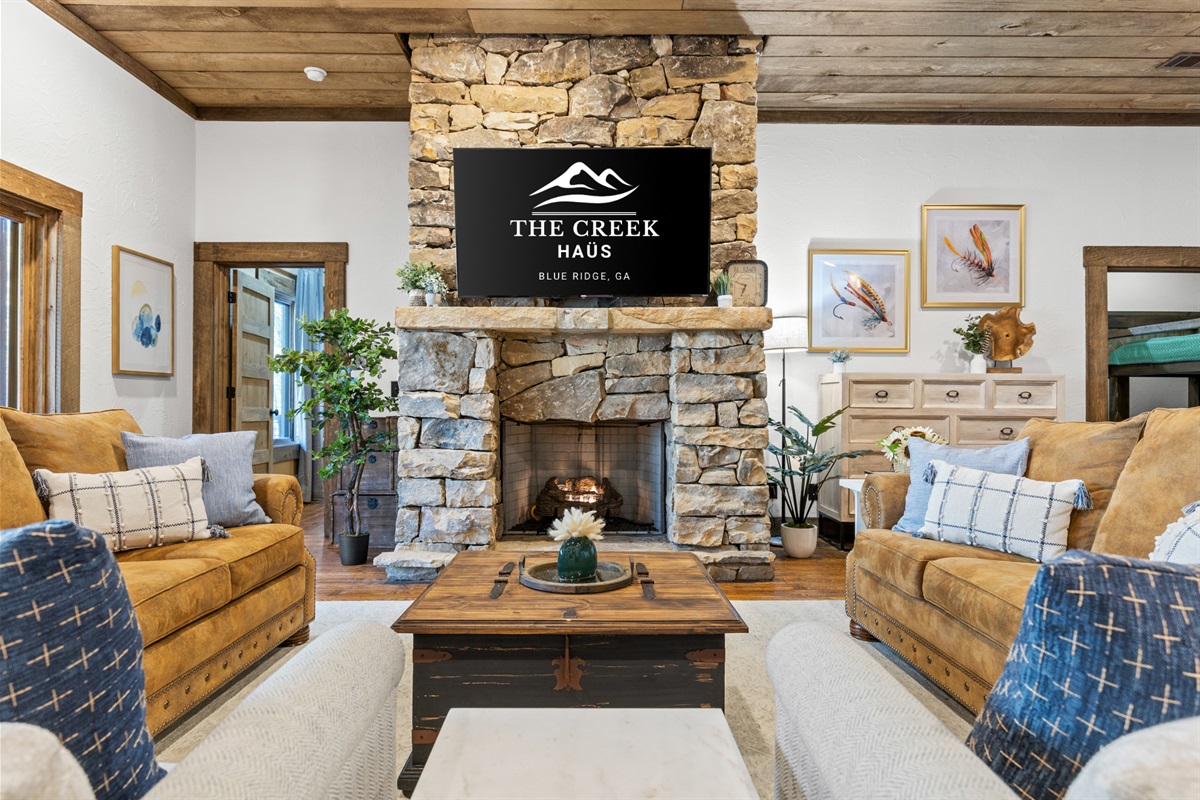 The lower level living room features a cozy stone fireplace, plush seating, and large windows that frame the serene outdoor views.
