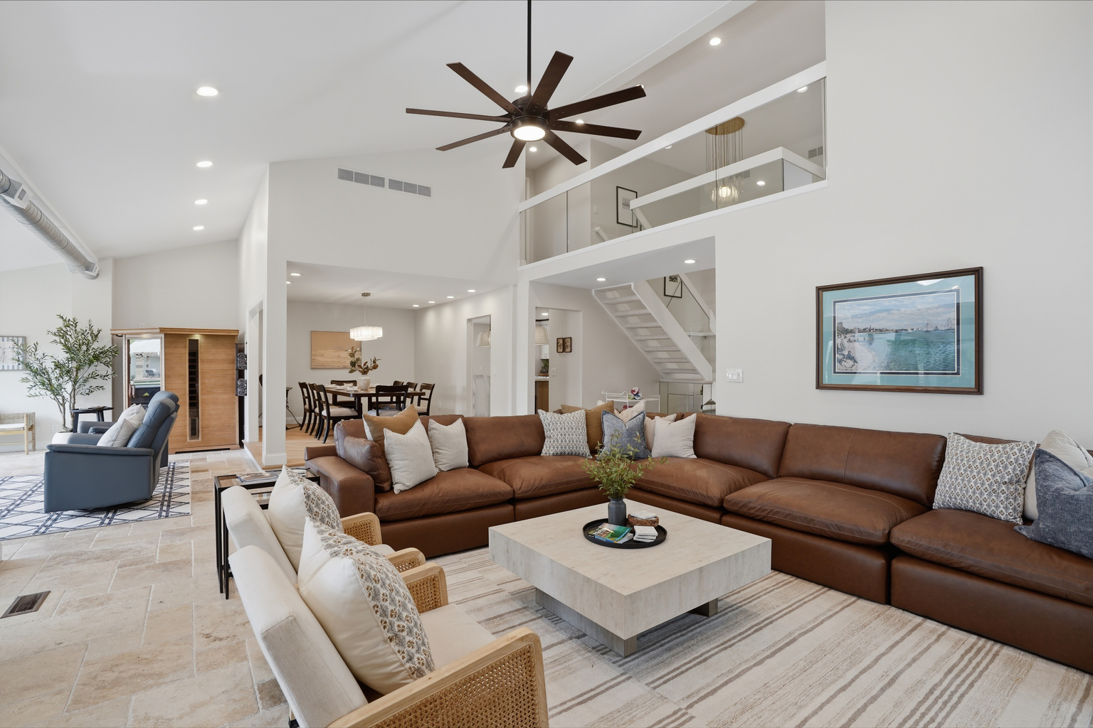 Gather with family and friends in this stunning open-concept living room, featuring soaring ceilings, a spacious sectional sofa, abundant natural light, and modern coastal-inspired design. The airy layout seamlessly connects the living, dining, and loft ar