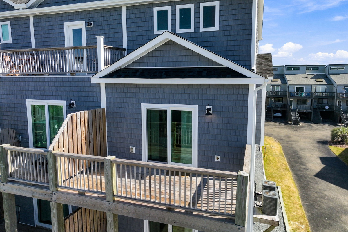 Elevated view of the private wooden deck featuring privacy partitions, sliding glass door entry, and scenic views of the coastal community.   