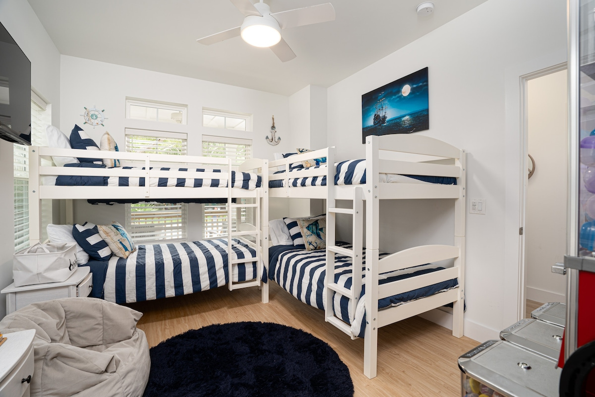 Two twin-over-twin bunks, striped navy bedding, and four children who will absolutely argue over who gets a top bunk. There is a beanbag in the corner and a TV on the wall for the hour after the beach.