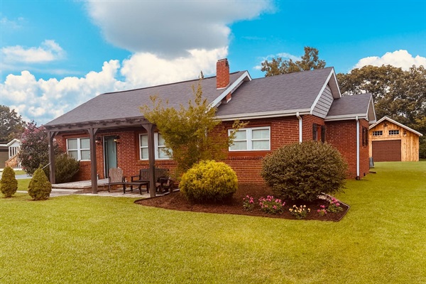 This inviting brick cottage features a cozy front porch with rocker and bench seating, perfect for morning coffee or evening relaxation. Surrounded by a spacious yard, as well as large back patio, it offers the perfect blend of comfort and charm. 